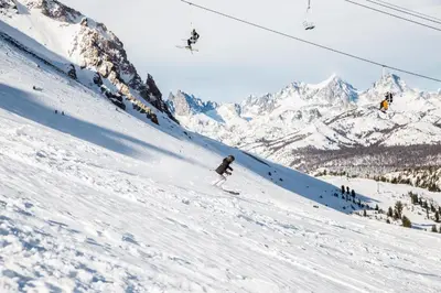 a person skiing down a snow covered slope with a ski lift at Silver Bear #22 condo in Mammoth Lakes