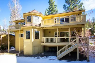 a large yellow house with a deck in the snow at Skidder Trail Family Lodge home in Truckee