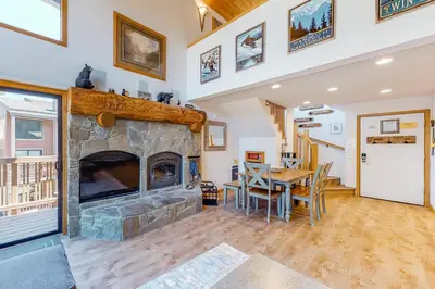 a living room with a stone fireplace and a table at Summit 70 in Mammoth Lakes
