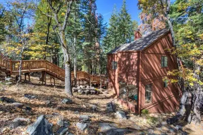 a cabin in the woods with a deck and a bench at Forest Glen in Yosemite West