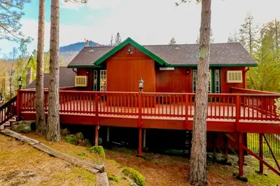 a red house with a large deck in the woods at Calandri Lakeview House in Bass Lake