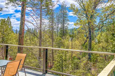 a balcony with a table and chairs and a view of the forest at Alford Family Lodge in Bass Lake
