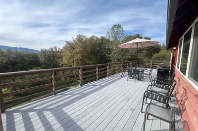 a deck with a table and chairs and an umbrella at Hodges Hill Yosemite House in Oakhurst