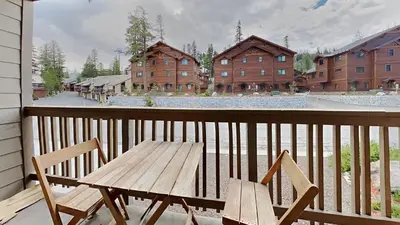 a wooden table and chairs on a balcony with buildings at Spacious One Bedroom Condo in Mammoth! Free Assigned Parking - Snowbird 107 in Mammoth Lakes