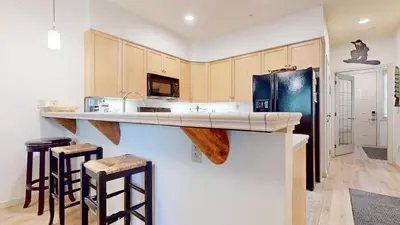 a kitchen with a counter and a refrigerator and stools at Mammoth Green 118 Located on Sierra Star Golf Course, Private Patio, Summer Pool condo in Mammoth Lakes