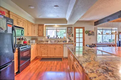a large kitchen with wooden cabinets and a black refrigerator at Gorgeous Oakhurst Retreat with Swimming Hole! in Oakhurst