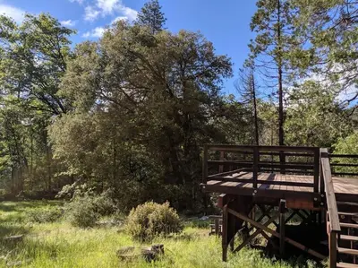 a wooden deck in a field with trees in the background at Gilmore Cabin in Miramonte