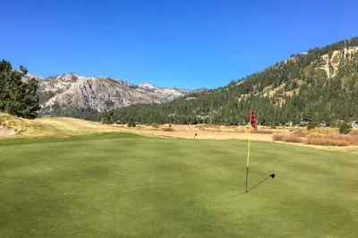 a golf club on a green with mountains in the background at Resort at Squaw Creek's 560 & 558 in Olympic Valley