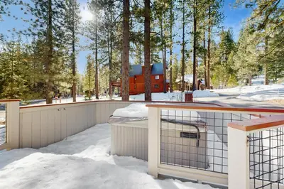 a snow covered deck with a red house in the background at Northstar Home in Truckee