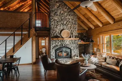 a living room with a stone fireplace in a log cabin at Scenic View Timber Lodge HotTub by Casa Oso in Mariposa