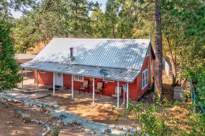 a red house with a metal roof in the woods at Acorn Cabin - Charming Place, Your getaway to Yosemite, Bass Lake in Oakhurst