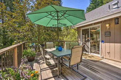 a table and chairs with a green umbrella on a deck at 1 Mi to Jenkinson Lake Apples Chalet with Deck in Pollock Pines