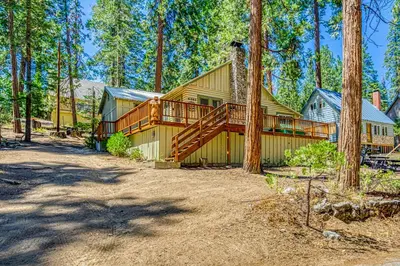 a large house with a deck in the woods at Alpine Cottage in Shaver Lake