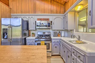 a kitchen with white cabinets and stainless steel appliances at Lovely Oakhurst Cabin with Deck and Mtn Views! in Oakhurst