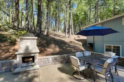 a patio with a fireplace and a table with an umbrella at 12 Mi to Apple Hill Family-Friendly Cabin Retreat in Pollock Pines