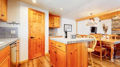 a kitchen with wooden cabinets and a dining room with a table at Mammoth Sierra Townhomes #18 condo in Mammoth Lakes