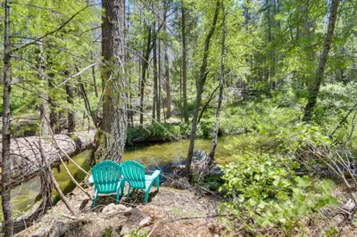 two chairs sitting next to a river in the woods at 7 Mi to Yosemite Natl Park Riverfront Getaway! in Groveland