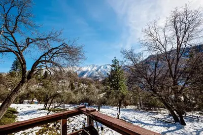 a wooden deck in the snow with mountains in the background at Hygge Haus Sequoia - Large Private Cabin w Views in Ponderosa