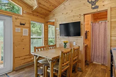 a dining room with a wooden table and chairs and a flat screen tv at Adorable little cabin #21 in Kernville