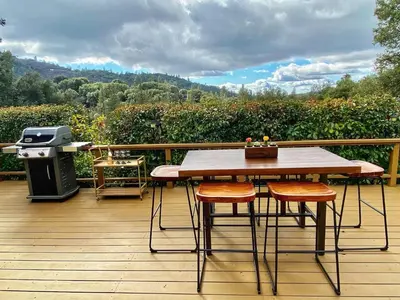 a wooden deck with a table and chairs and a grill at Cozy Cabin Near Yosemite & Bass lake, Breathtaking Views & Private Hot Tub, BBQ, Nature Getaway in Oakhurst