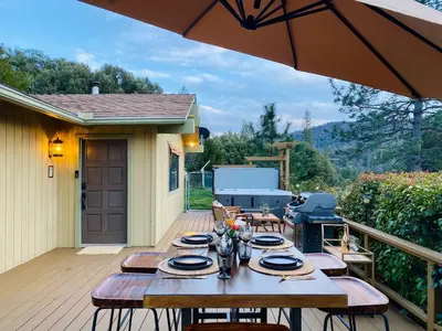 a wooden table on a deck with an umbrella at Cozy Cabin Near Yosemite & Bass lake, Breathtaking Views & Private Hot Tub, BBQ, Nature Getaway in Oakhurst