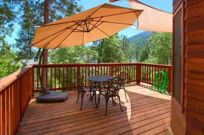 a wooden deck with a table and chairs and an umbrella at Willow Cove Lodge- 5 bedrooms with a hot tub in Bass Lake