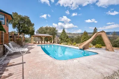 a swimming pool with a slide next to a house at Yosemite Adventure House with Pool-hot tub-game room in Oakhurst