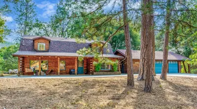 a log cabin in the woods with trees at Log Cabin w/ pool, spa, game room, sleeps 20 in Coarsegold