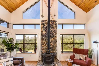 an open living room with a fireplace and windows at Hilltop Haven- Bright and Modern Cabin w/ hot tub and stunning views in Oakhurst