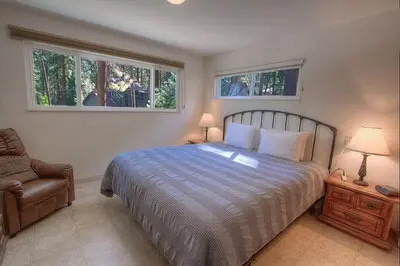 a bedroom with a bed and a chair and two windows at Foothill Folly home in Zephyr Cove