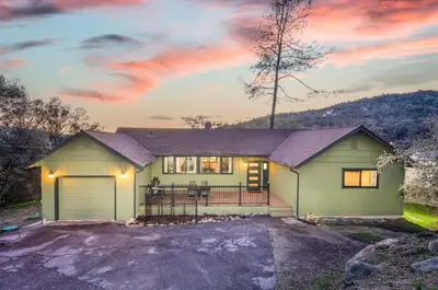 a house with a garage at sunset at Buckeye Bungalow w hot tub/firepit/views Pet Friendly in Oakhurst