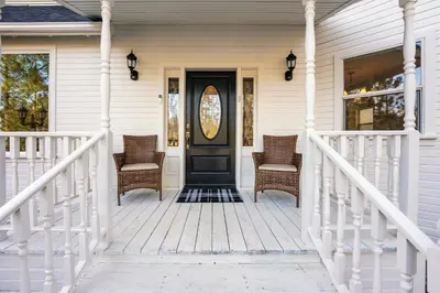 a front porch with wicker chairs and a black door at Yosemite Country House sleeps 20 w/ hot tub, firepit, bonus studio in Oakhurst