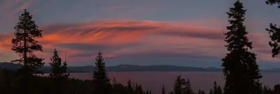 a sunset over a lake with trees in the foreground at Carnelian Bay View Cabin in Carnelian Bay